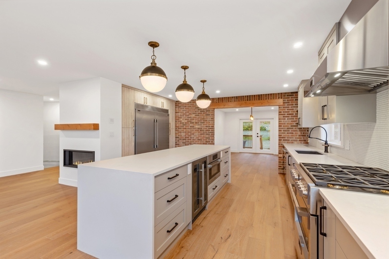 Modern kitchen with large island, stainless steel appliances, brick accent wall, and hardwood flooring